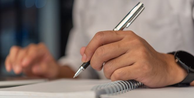 Corrección Bilingüe-Businessperson reading and writing on book.education studying knowledge development and cognition learning concept. Pantalla con documento siendo corregido en inglés y español